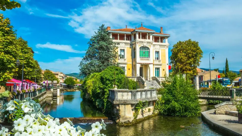 A picturesque scene of a grand building by a tree-lined canal under a clear blue sky.