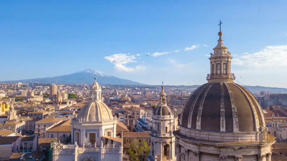 A cityscape featuring historic domes with a mountain in the background under a clear blue sky.