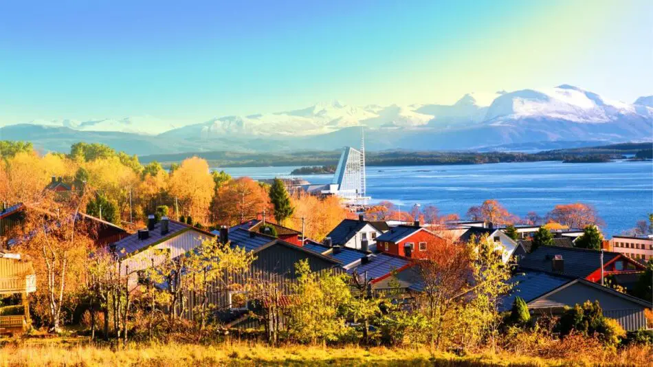 Colorful houses surrounded by autumn trees with a view of a lake and snow-capped mountains in the background.