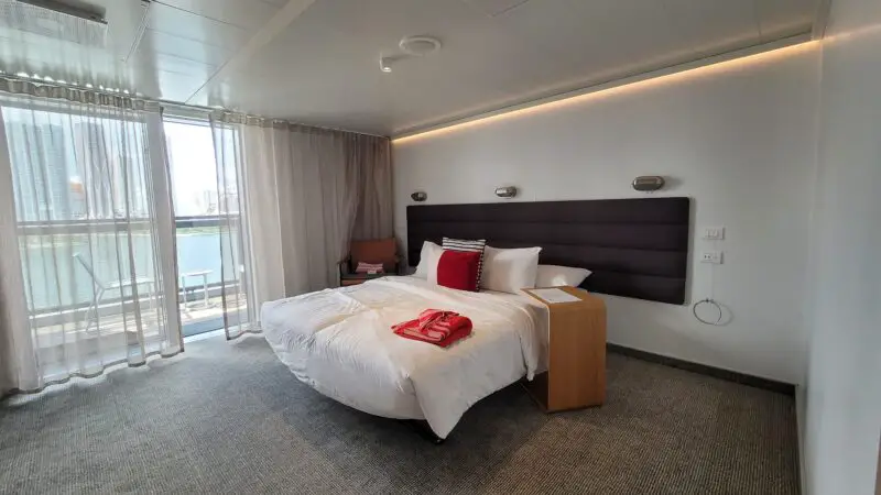 Cruise ship cabin with a bed, side table, and balcony view through sheer curtains.