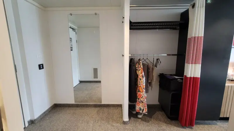 Virgin Voyages cruise ship cabin with open wardrobe, patterned clothing on hangers, and a mirror on the wall.