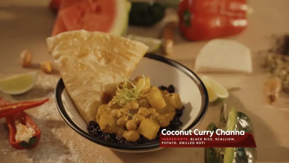 Bowl of coconut curry channa with potatoes over black rice and roti