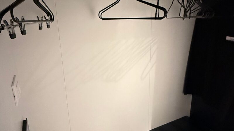 View of a Virgin Voyages cruise ship cabin closet, featuring several coat hangers on a rail and a small shelf unit below.