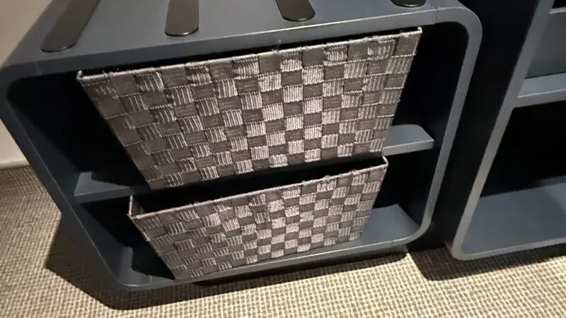 Dark shelf unit with woven storage baskets in a Virgin Voyages cruise ship cabin.