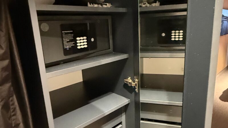 Interior of a Virgin Voyages cruise ship cabin showing an open wardrobe with life jackets and a safe.