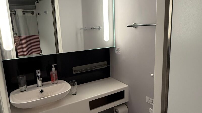 Modern Virgin Voyages cruise ship cabin bathroom with a sink, mirror, and toilet.