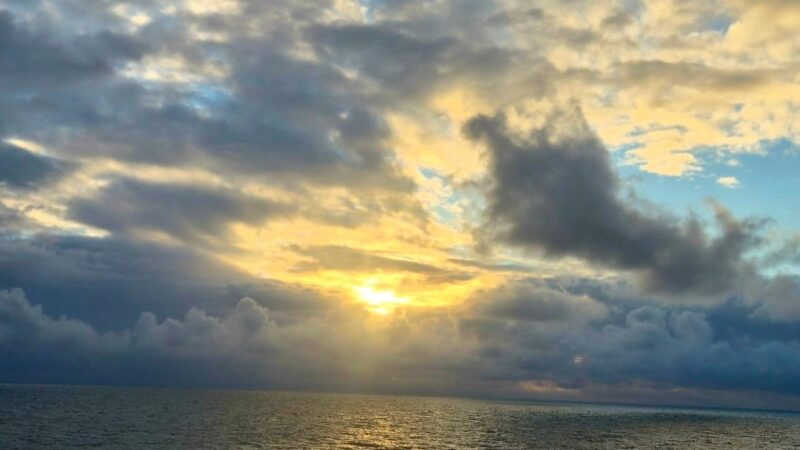 A view of the ocean with a sunset and clouds, seen from a Virgin Voyages cruise ship balcony.