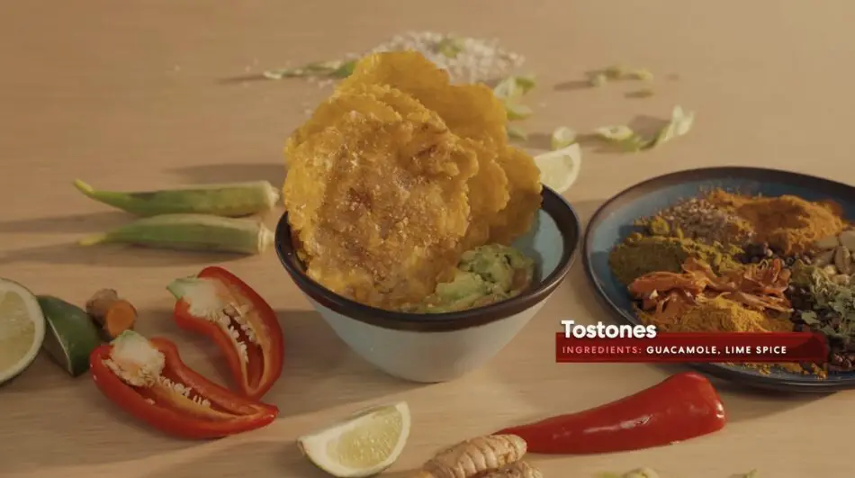 Bowl of crispy tostones with guacamole surrounded by lime wedges and peppers