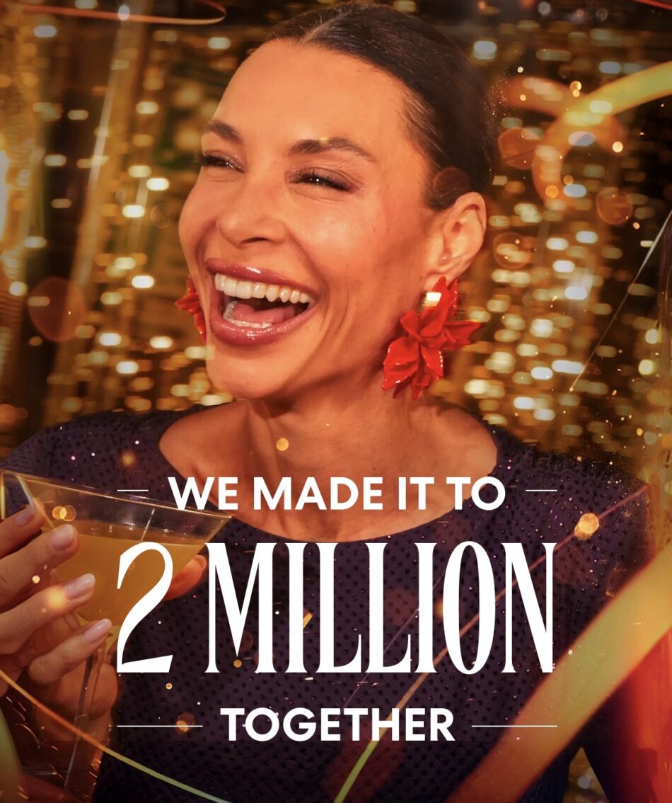 Smiling woman with red floral earrings holding a drink at a celebration, We made it to 2 million together