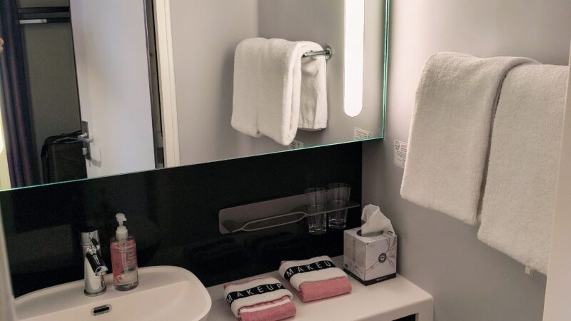 Cruise ship cabin bathroom with a sink, mirror, towels, toiletries, and a toilet.