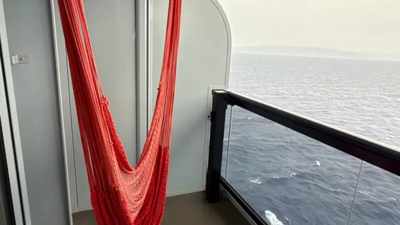 A Virgin Voyages cruise ship balcony with a red hammock and ocean view.