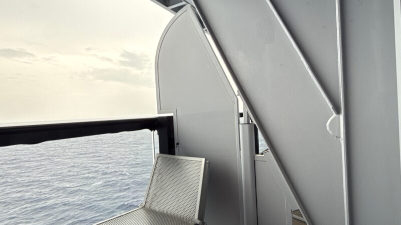 A Virgin Voyages cruise ship balcony with a perforated metal chair, overlooking the ocean.