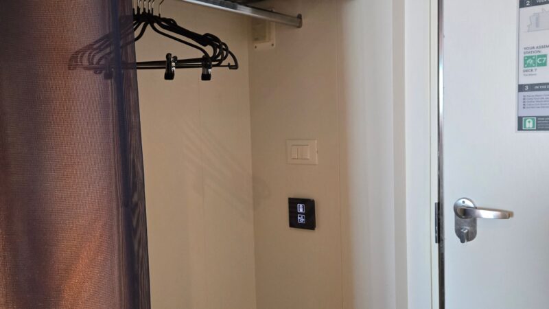 Virgin Voyages cruise ship cabin entrance with a closet area featuring hangers, a shelf, and a privacy curtain.