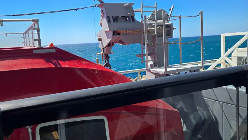 View from a Virgin Voyages cruise ship balcony, overlooking a bright blue sea with a part of the ship’s exterior structure visible.