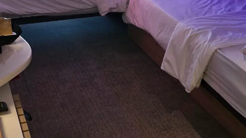 Virgin Voyages cruise ship cabin featuring twin beds with white linens, a leather chair, and a window with sheer curtains leading to a balcony.