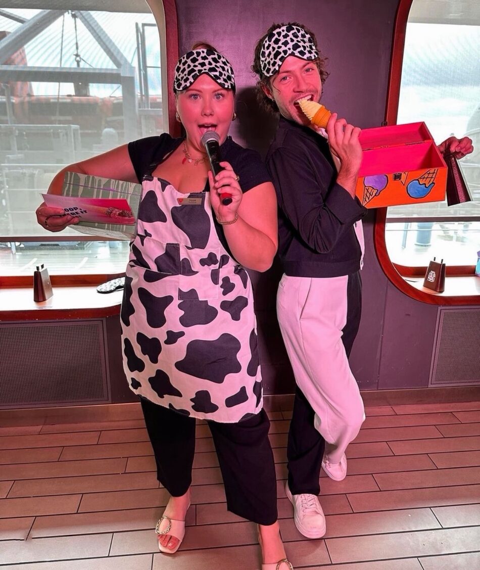 Two entertainers in cow-print outfits with sleep masks perform on a Virgin Voyages cruise ship