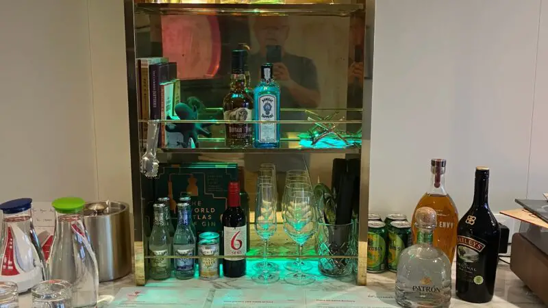A Virgin Voyages cruise ship cabin minibar with an assortment of liquor bottles, glassware, and a marble countertop.