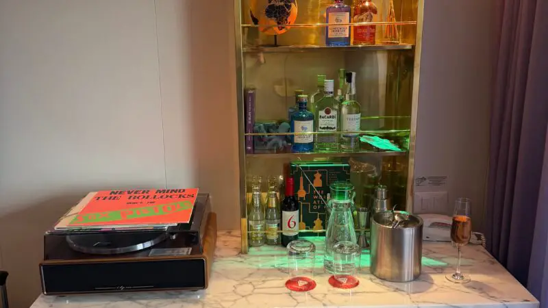 Cruise ship cabin featuring a marble-topped bar with various bottles, a record player with a vinyl record, and a glass of champagne.